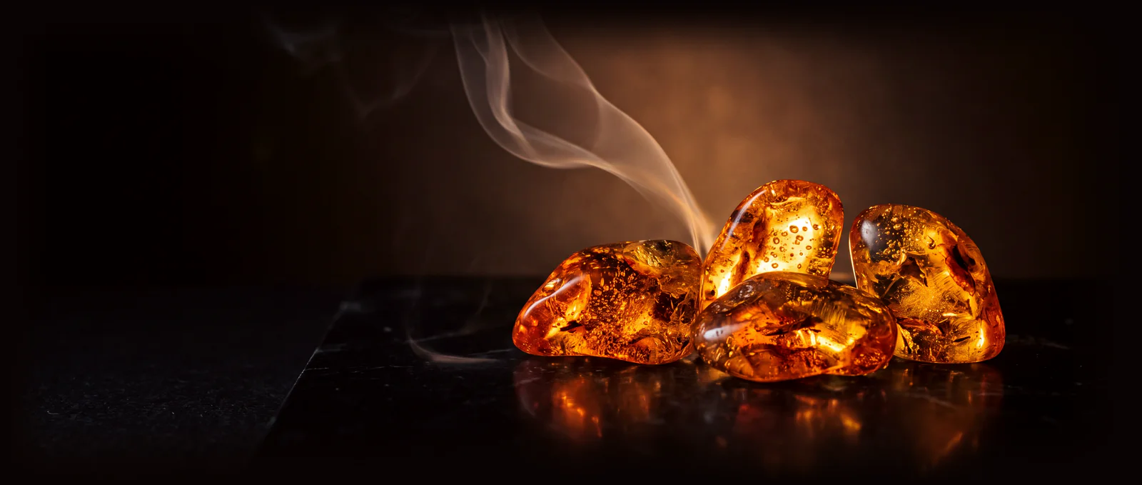 Pieces of amber resin glowing like embers on black stone, a ribbon of smoke rising through the light.